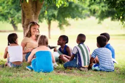 A lady teacher is teaching students under a tree
